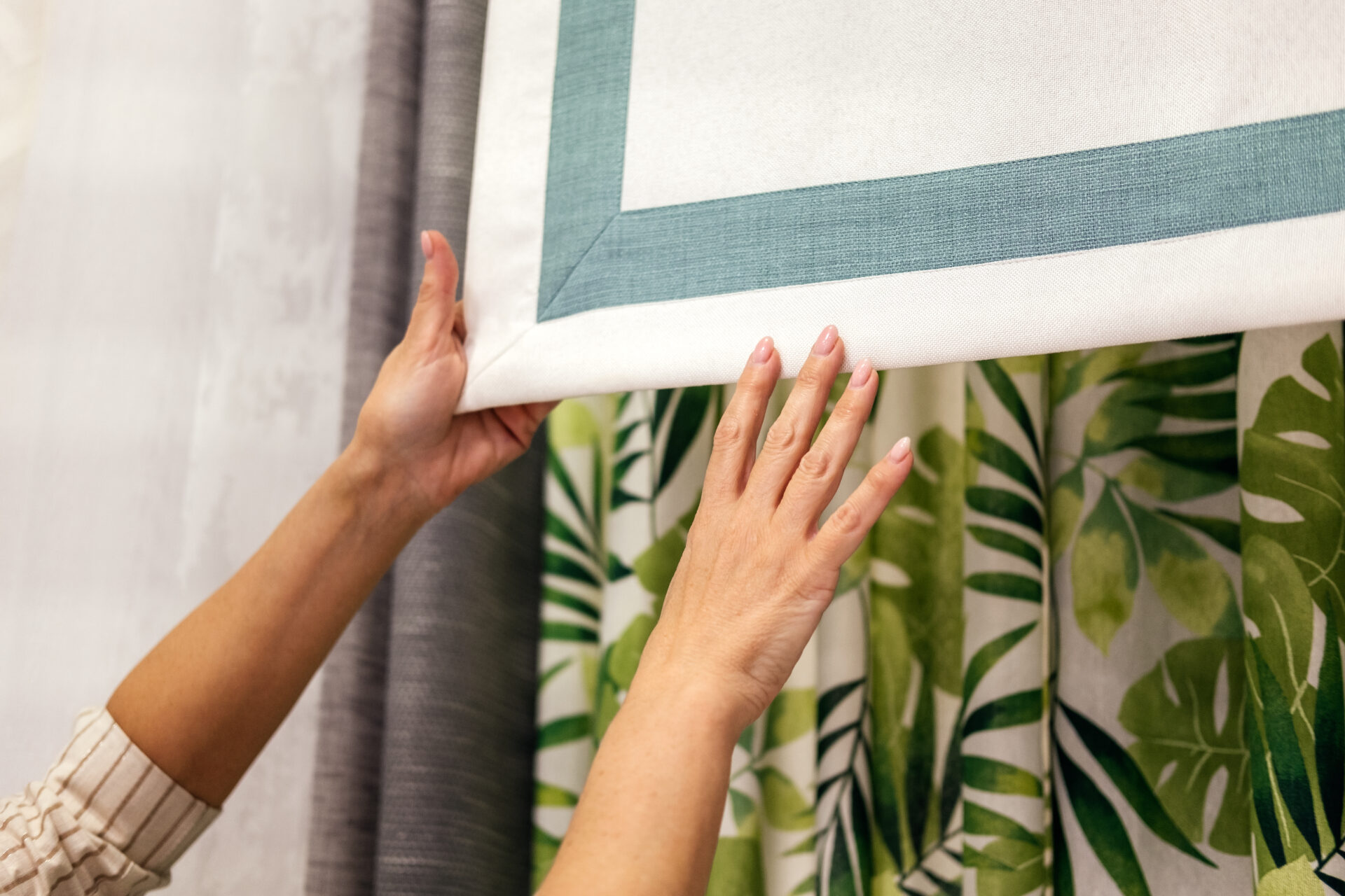 Female hands choosing fabric for curtain indoor. Woman designer combining colors and textures in studio